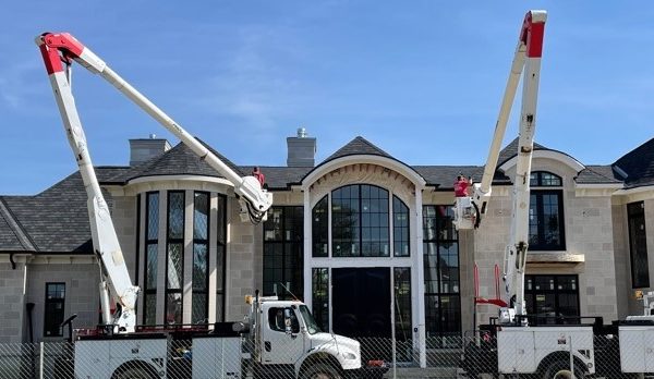 A large hydraulic lift crane with red and white arms extended, parked in front of a commercial building with arched windows and a peaked roof.